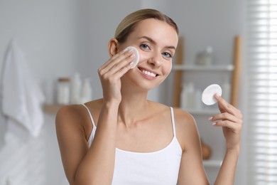 Photo of Smiling woman removing makeup with cotton pads in bathroom