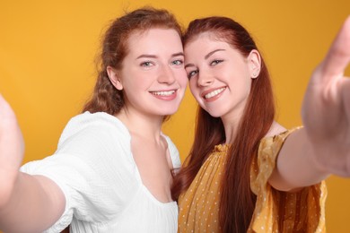 Photo of Beautiful young redhead sisters taking selfie on orange background