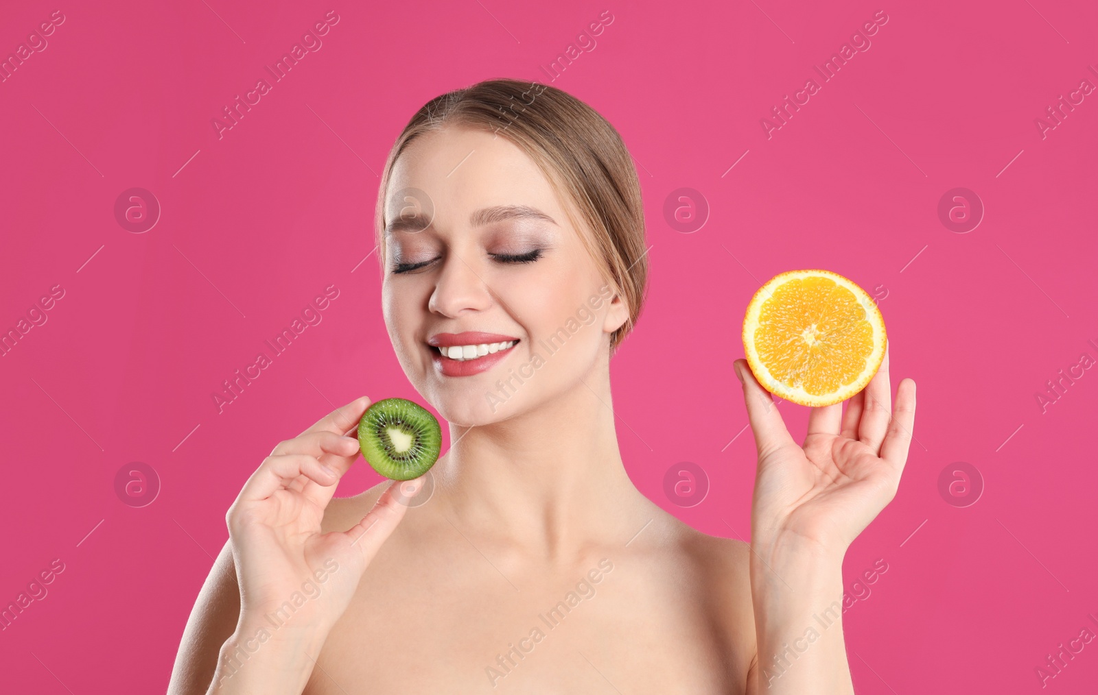 Photo of Young woman with cut kiwi and orange on pink background. Vitamin rich food