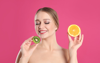 Young woman with cut kiwi and orange on pink background. Vitamin rich food