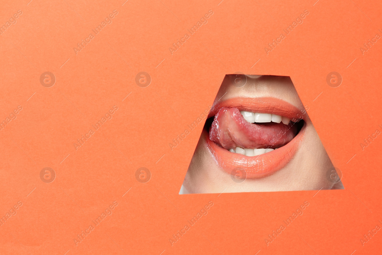 Photo of Lips of young woman with beautiful lipstick visible through hole in color paper. Space for text