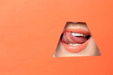 Photo of Lips of young woman with beautiful lipstick visible through hole in color paper. Space for text