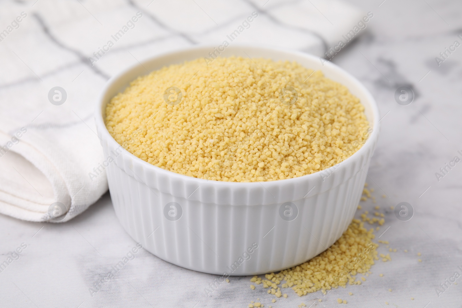 Photo of Raw couscous in bowl on light table, closeup