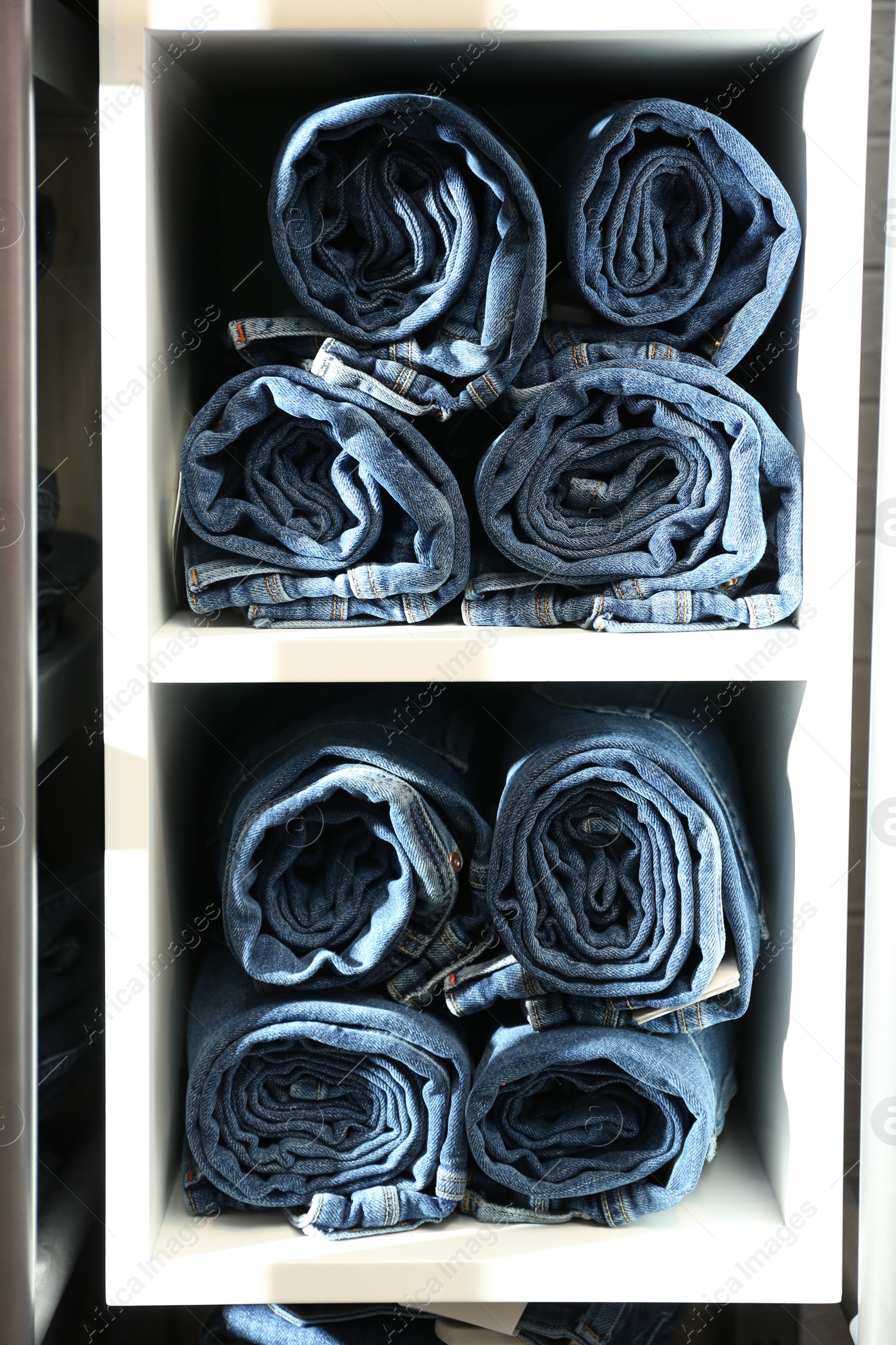 Photo of Collection of stylish jeans on shelves in shop