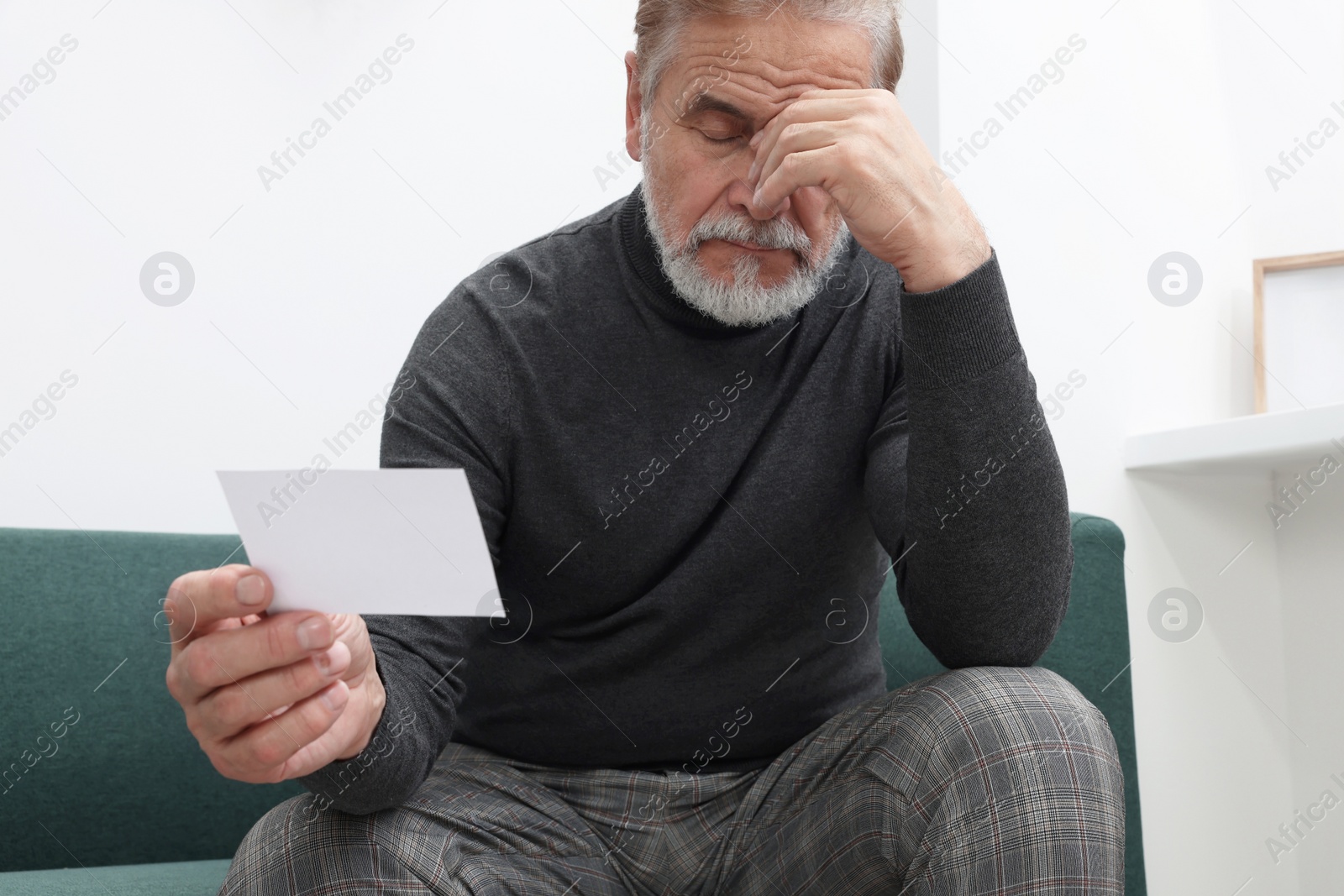 Photo of Upset senior man holding photo on sofa at home. Loneliness concept