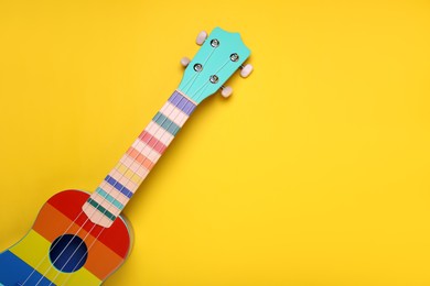 Photo of Colorful ukulele on yellow background, top view with space for text. String musical instrument