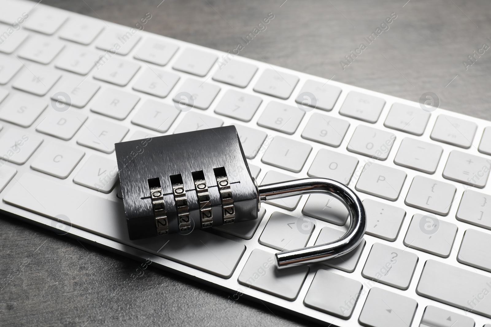 Photo of Cyber security. Metal combination padlock and keyboard on grey table, closeup