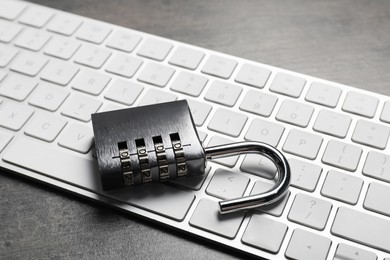 Photo of Cyber security. Metal combination padlock and keyboard on grey table, closeup
