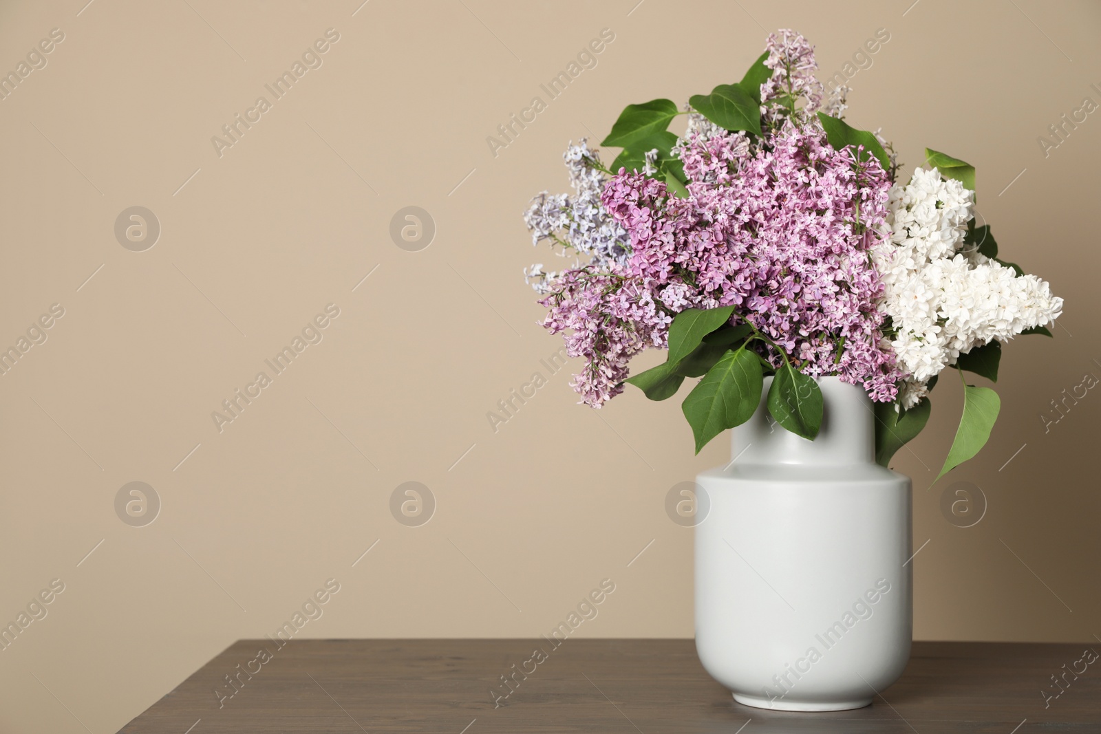 Photo of Beautiful lilac flowers in vase on wooden table against beige background. Space for text