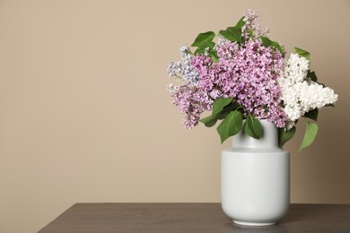 Beautiful lilac flowers in vase on wooden table against beige background. Space for text