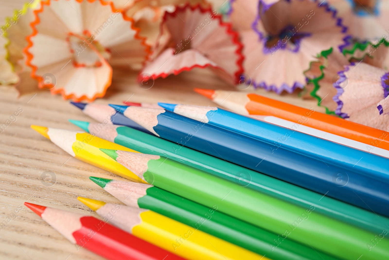 Photo of Color pencils and shavings on wooden table, closeup