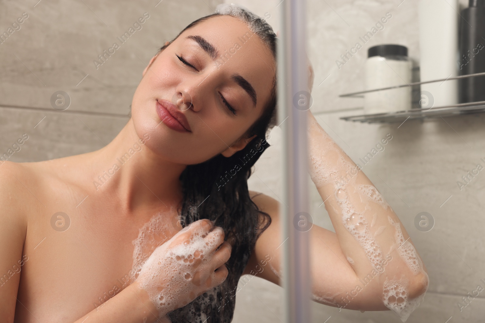 Photo of Beautiful woman washing hair with shampoo in shower