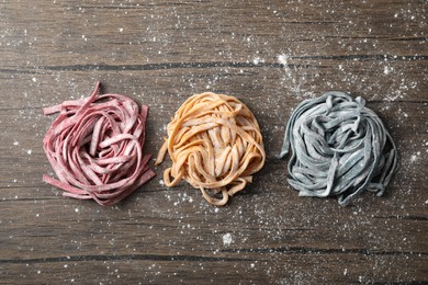 Photo of Rolled pasta painted with food colorings and flour on wooden table, flat lay
