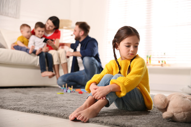 Unhappy little girl feeling jealous while parents spending time with other children at home