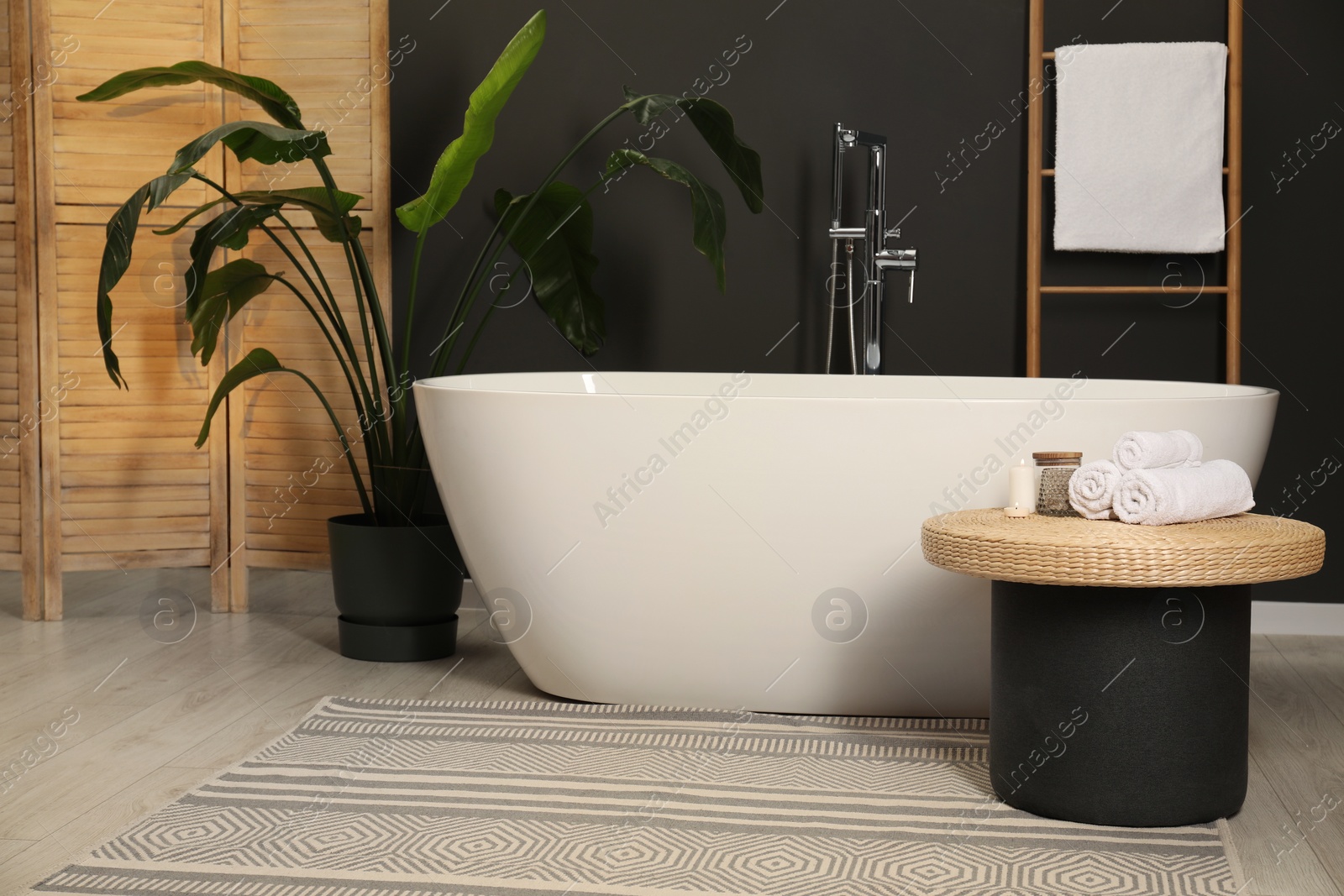 Photo of Spa day. Ceramic tub, houseplant and wicker table in bathroom