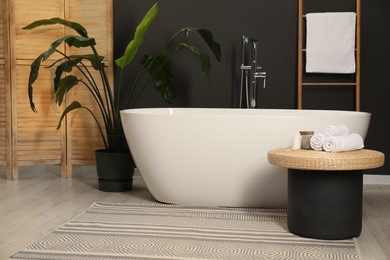 Spa day. Ceramic tub, houseplant and wicker table in bathroom