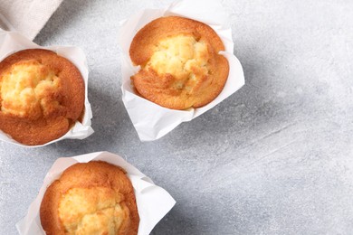 Photo of Delicious sweet muffins on light grey textured table, flat lay. Space for text