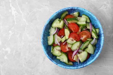 Bowl of vegetarian salad with cucumber, tomato and onion on marble background, top view. Space for text