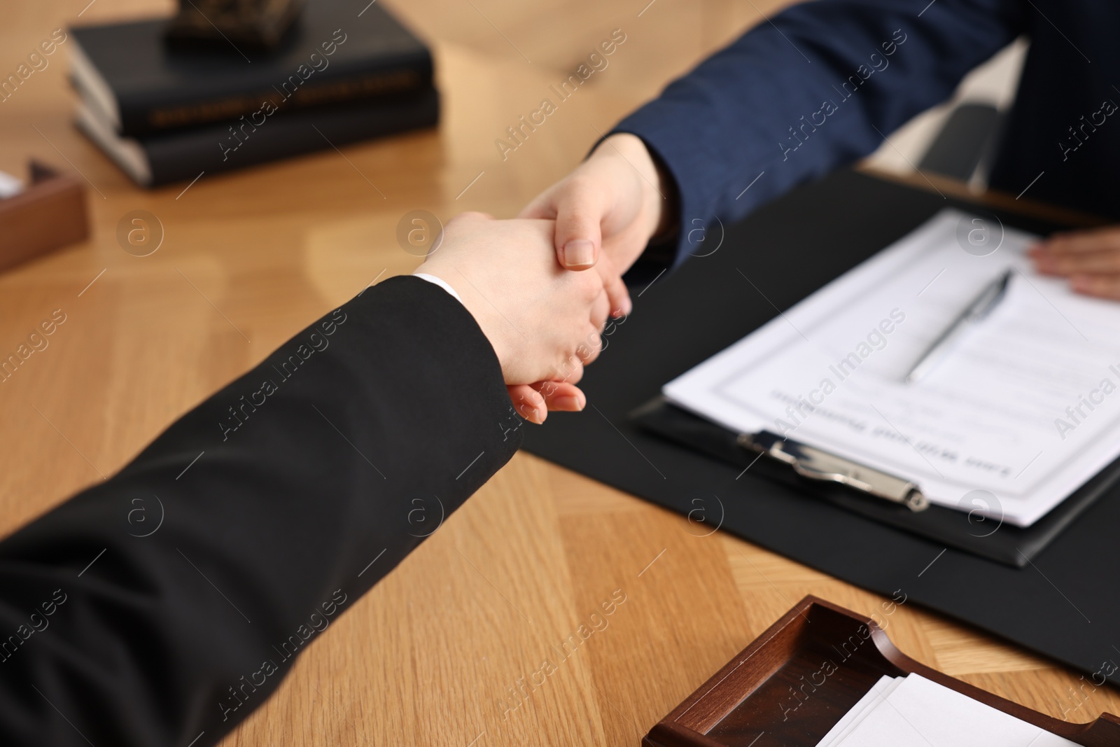 Photo of Notary shaking hands with client at wooden table in office, closeup