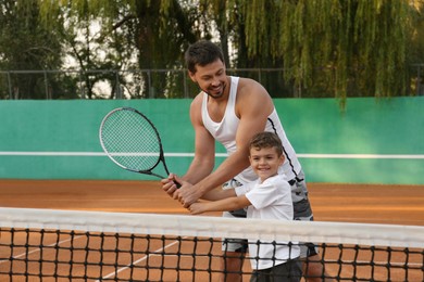 Father teaching son to play tennis on court