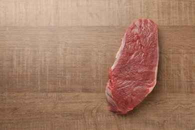 Photo of Piece of raw beef meat on wooden table, top view. Space for text