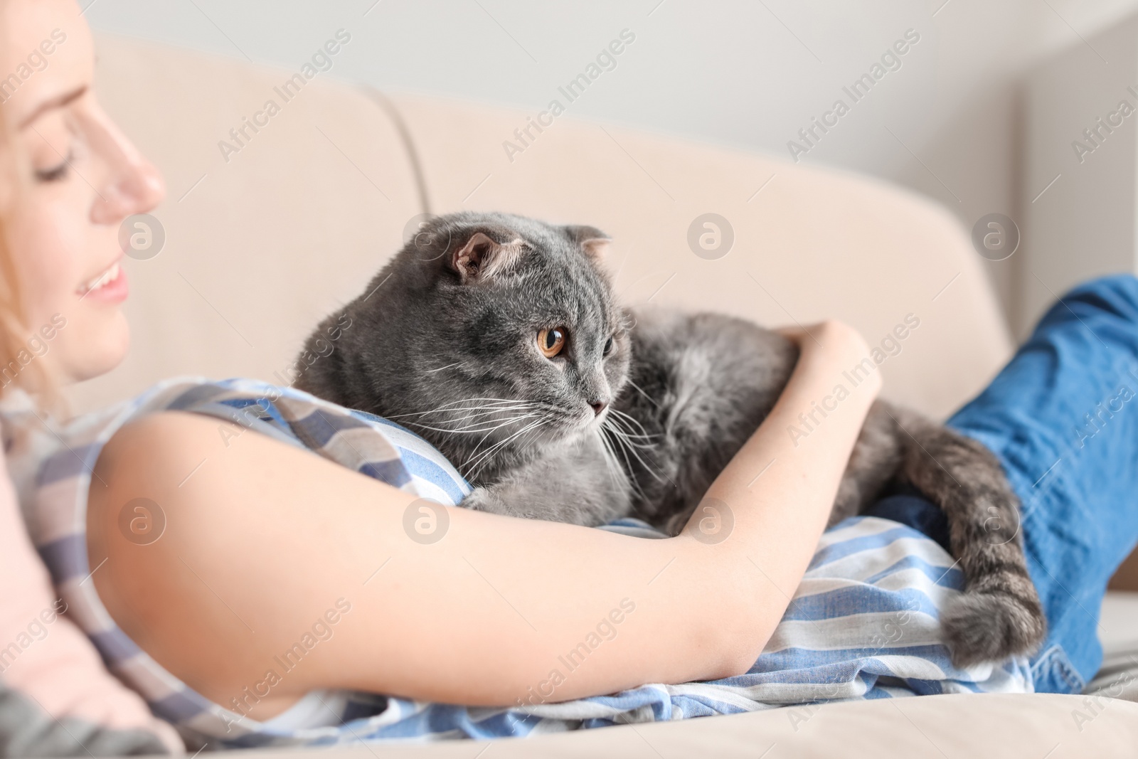 Photo of Young woman with her cute pet cat on sofa at home