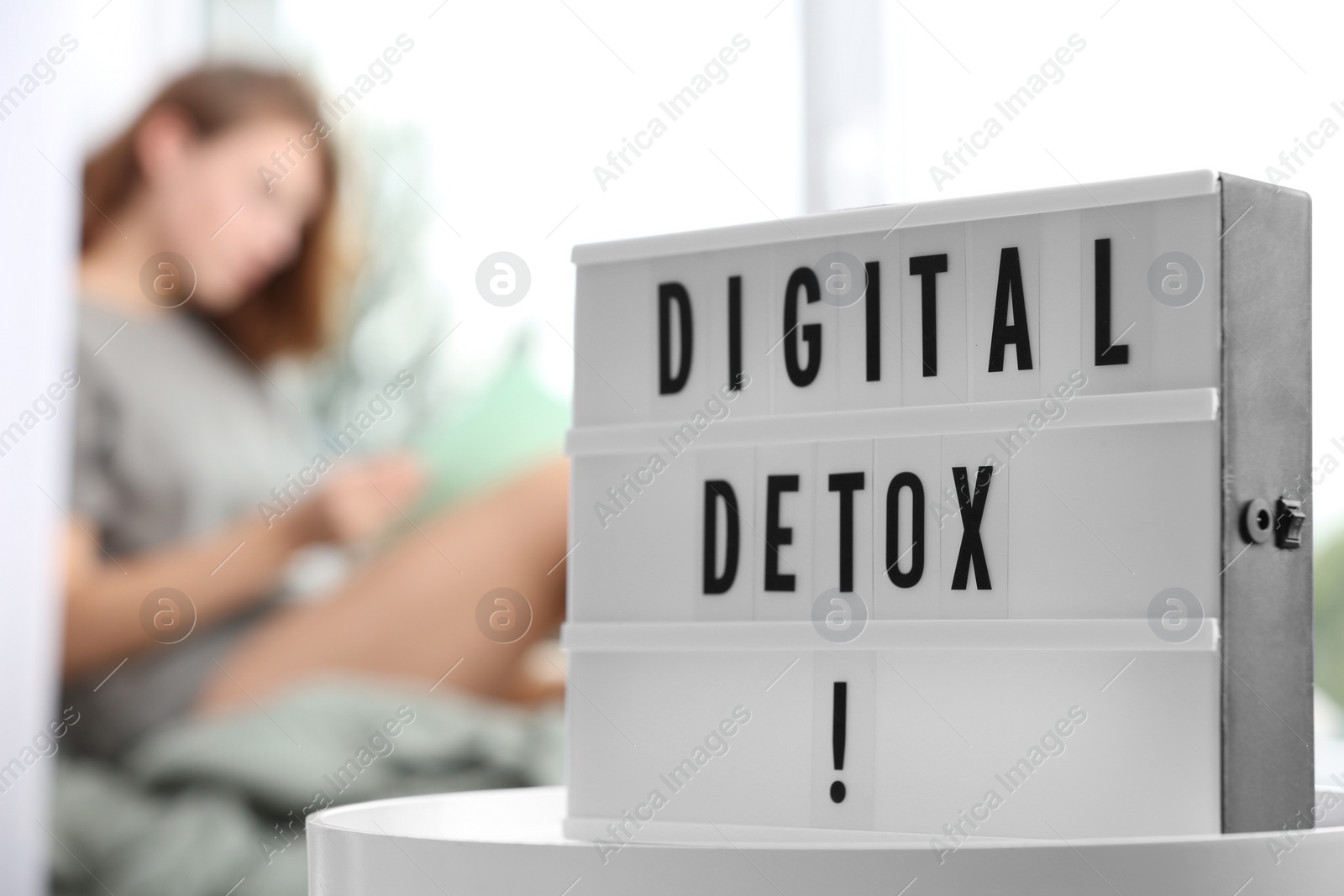 Photo of Woman resting near window at home, focus on lightbox with phrase DIGITAL DETOX