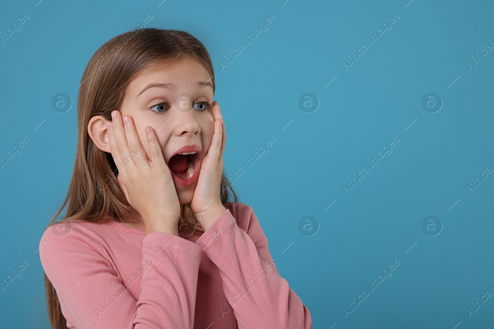 Photo of Portrait of surprised girl on light blue background. Space for text