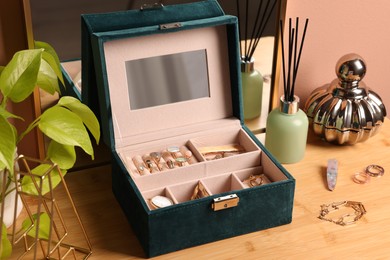 Photo of Elegant jewelry box with beautiful bijouterie and expensive wristwatch on wooden table