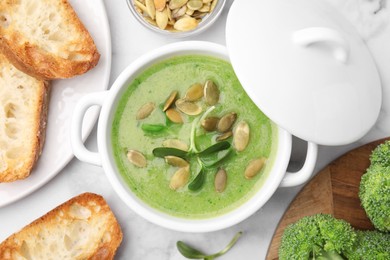 Photo of Delicious broccoli cream soup with pumpkin seeds on white marble table, flat lay