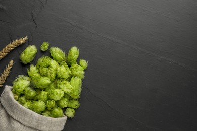 Photo of Sack with fresh green hops and spikes on black table, flat lay. Space for text