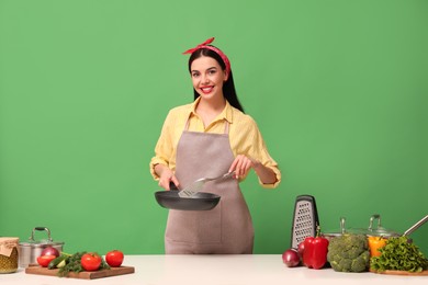 Young housewife with vegetables and different utensils on green background