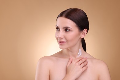 Photo of Beautiful woman with smear of body cream on her neck against light brown background, space for text