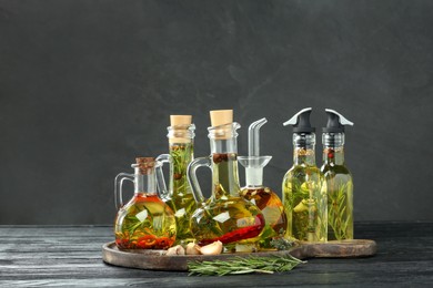 Photo of Cooking oil with different spices and herbs in bottles on grey wooden table