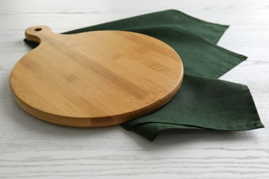 Photo of Empty wooden board and green napkin on white table, closeup