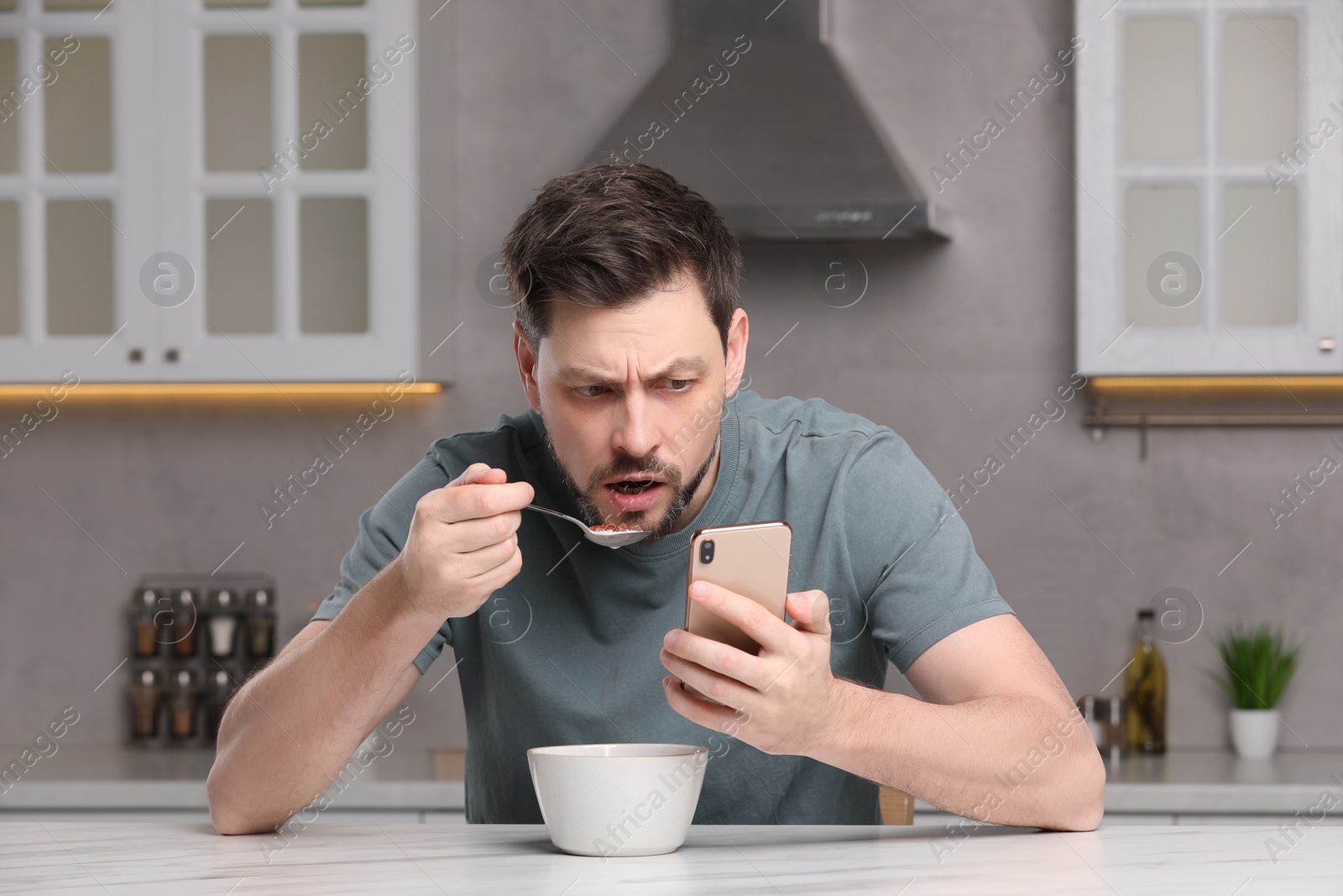 Photo of Man using smartphone while having breakfast at table in kitchen. Internet addiction