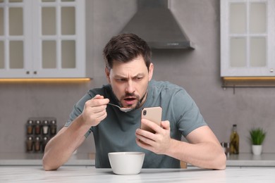Man using smartphone while having breakfast at table in kitchen. Internet addiction