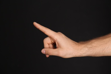 Man pointing at something on black background, closeup. Finger gesture