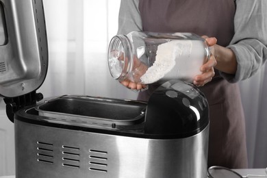 Photo of Woman adding flour into breadmaker at table indoors, closeup