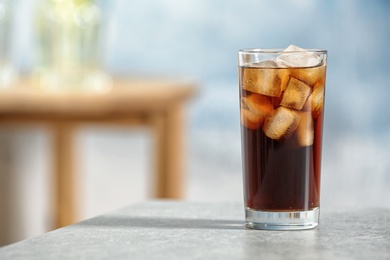 Photo of Glass of cold cola on table against blurred background. Space for text