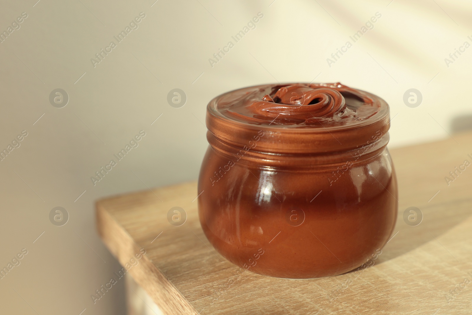 Photo of Glass jar with tasty chocolate hazelnut spread on wooden table. Space for text