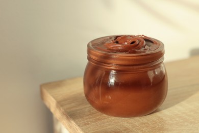 Photo of Glass jar with tasty chocolate hazelnut spread on wooden table. Space for text