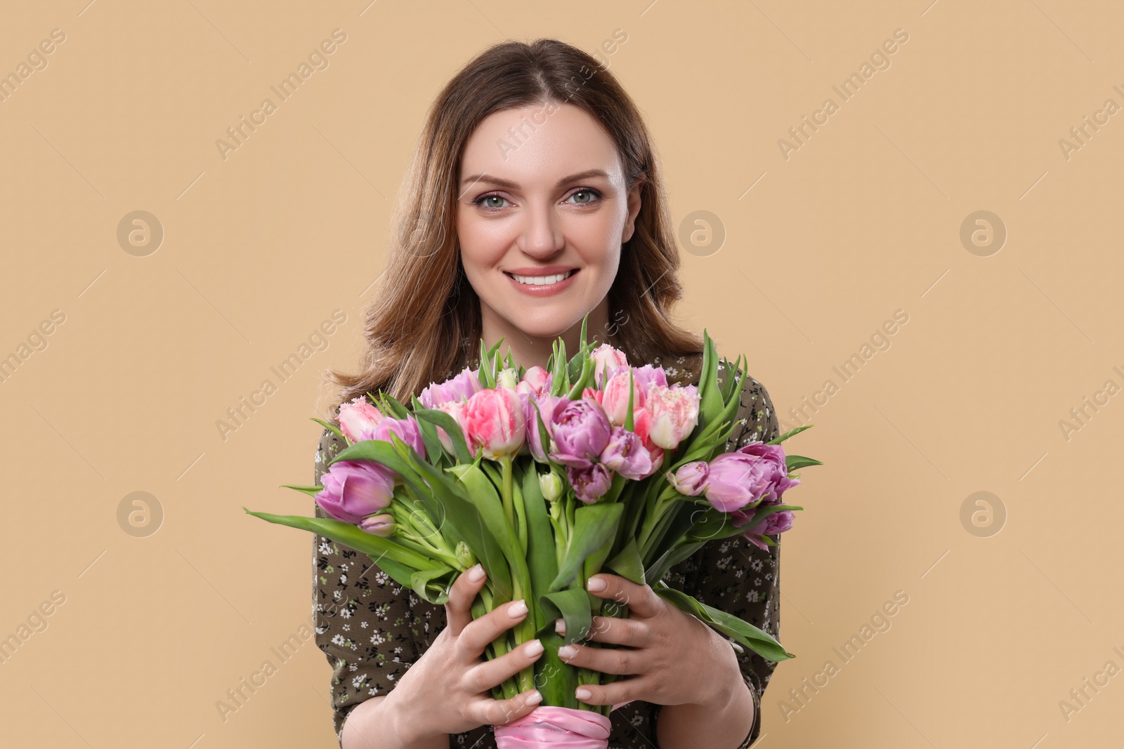 Photo of Happy young woman holding bouquet of beautiful tulips on beige background