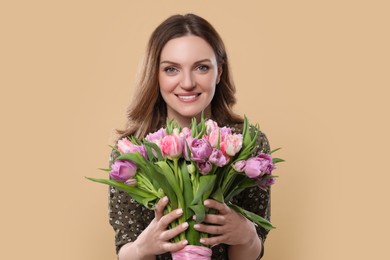 Happy young woman holding bouquet of beautiful tulips on beige background