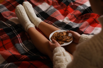 Photo of Woman in knitted socks with tasty cookies on warm plaid, closeup
