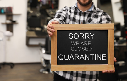 Image of Business owner holding sign with text SORRY WE ARE CLOSED QUARANTINE in barber shop, closeup
