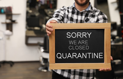 Business owner holding sign with text SORRY WE ARE CLOSED QUARANTINE in barber shop, closeup