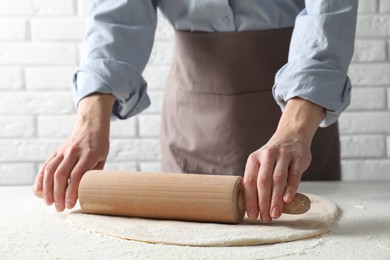 Woman rolling raw dough at table, closeup