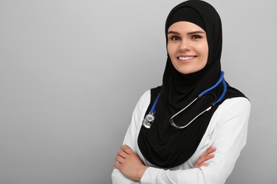 Photo of Muslim woman wearing hijab and medical uniform with stethoscope on light gray background, space for text