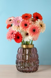 Photo of Bouquet of beautiful colorful gerbera flowers in vase on table against light blue background